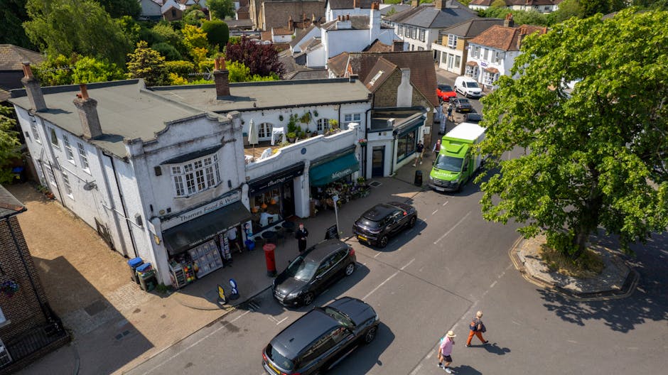 An aerial view of a busy street corner in Golders Green, featuring a white, two-story building with flower shops on the ground floor. The shop displays a green awning and has flower arrangements and p